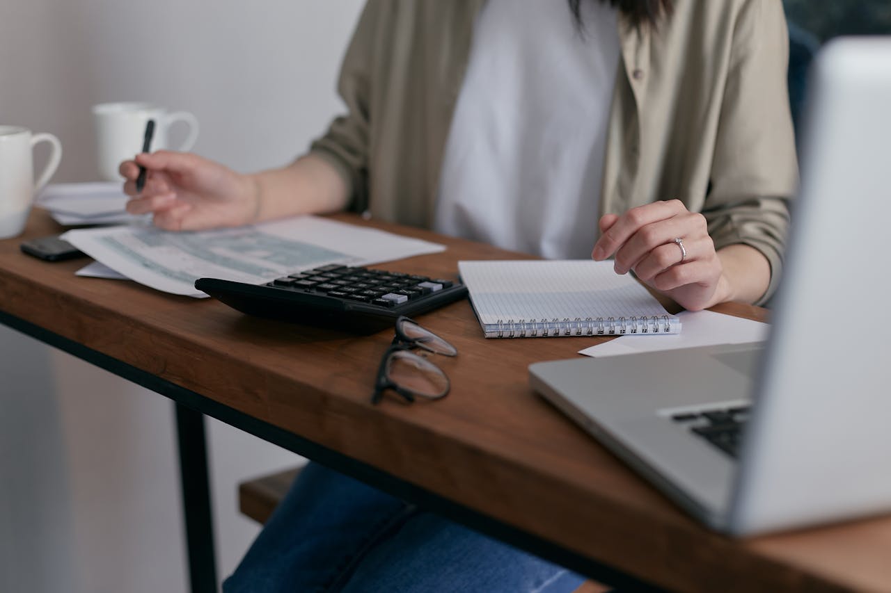 our-services-3 A woman manages finances at home, using a laptop and calculator on a wooden desk.